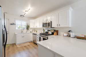 Kitchen with white cabinets, appliances with stainless steel finishes, light wood-style floors, a peninsula, and light stone countertops