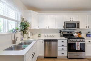 Kitchen featuring stainless steel appliances, white cabinets, and light stone counters