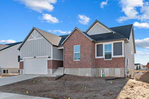 View of front of house with board and batten siding, roof with shingles, brick siding, and concrete driveway