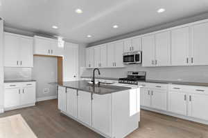 Kitchen with appliances with stainless steel finishes, white cabinetry, light wood finished floors, recessed lighting, and a kitchen island with sink