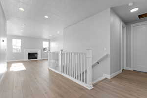 Corridor featuring recessed lighting, an upstairs landing, a textured ceiling, and light wood-style flooring