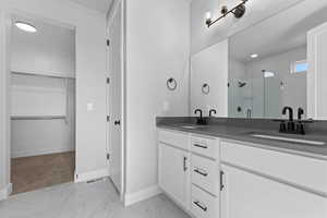 Bathroom with a walk in closet, a shower stall, double vanity, light marble finish floors, and recessed lighting