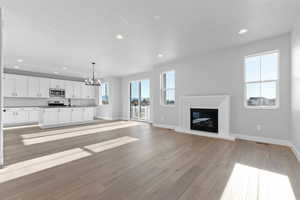 Unfurnished living room with recessed lighting, a glass covered fireplace, a chandelier, and light wood finished floors