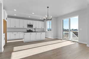 Kitchen featuring white cabinets, a chandelier, dark countertops, stainless steel appliances, and pendant lighting