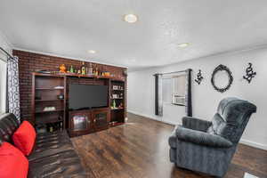 Living room with wood finished floors, brick wall, a textured ceiling, recessed lighting, and crown molding