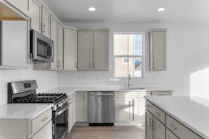 Kitchen with stainless steel appliances, gray cabinets, recessed lighting, light wood-style floors, and light stone counters