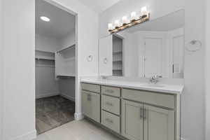 Full bathroom featuring double vanity, a spacious closet, light carpet, and light tile patterned floors