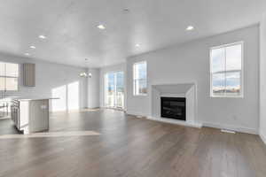 Unfurnished living room with a textured ceiling, a glass covered fireplace, recessed lighting, light wood-style flooring, and a chandelier