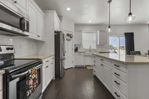Kitchen featuring stainless steel appliances, white cabinets, tasteful backsplash, pendant lighting, and dark wood-style floors