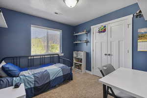 Bedroom with light carpet, a textured ceiling, and a closet