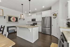 Kitchen featuring stainless steel appliances, backsplash, white cabinetry, a kitchen island, and a kitchen bar