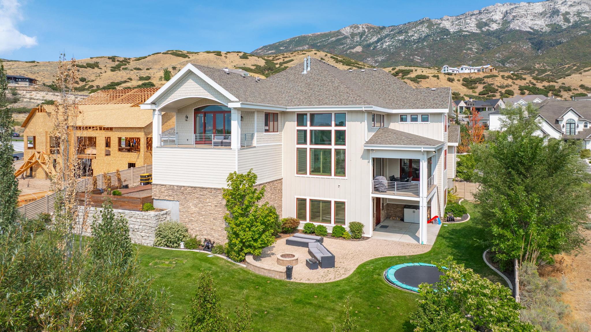 Back of property featuring a balcony, a patio, stone siding, a mountain view, and a shingled roof