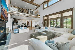 Living area featuring a glass covered fireplace, healthy amount of natural light, beam ceiling, recessed lighting, and carpet floors
