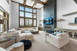 Carpeted living room with a high ceiling, a ceiling fan, a fireplace, beamed ceiling, and coffered ceiling