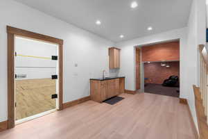 Bar featuring light wood-type flooring, brick wall, recessed lighting, and dark stone countertops