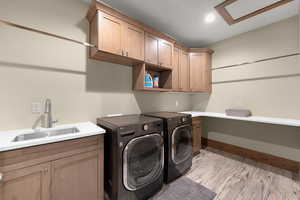 Laundry room with light wood-style flooring, washer and dryer, and cabinet space