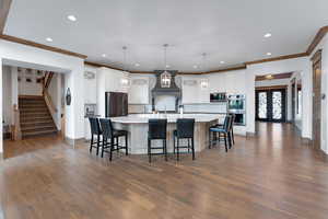 Kitchen with a large island, a breakfast bar, white cabinetry, hanging light fixtures, and dark wood-style flooring
