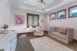 Bedroom featuring a crib, a raised ceiling, dark carpet, wallpapered walls, and ceiling fan
