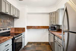 Kitchen featuring gray cabinets, appliances with stainless steel finishes, backsplash, dark stone finish floors, and glass insert cabinets
