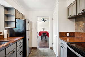 Kitchen featuring freestanding refrigerator, stone tile flooring, tasteful backsplash, gray cabinets, and crown molding