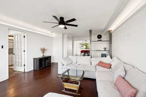 Living area featuring dark wood-style floors, ceiling fan, and crown molding