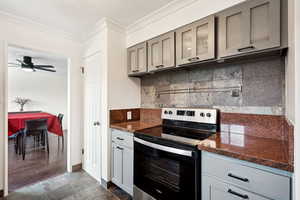 Kitchen with range with electric cooktop, decorative backsplash, gray cabinets, ornamental molding, and dark stone countertops