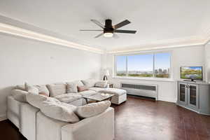 Living room with radiator, a ceiling fan, crown molding, and dark floors