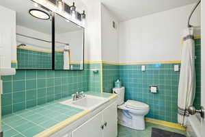 Full bath with tile patterned floors, tile walls, vanity, and a wainscoted wall
