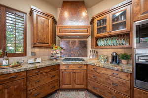 Kitchen featuring brown cabinets, premium range hood, backsplash, and appliances with stainless steel finishes