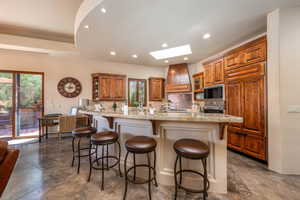 Kitchen with brown cabinets, a skylight, a kitchen breakfast bar, tasteful backsplash, and open shelves