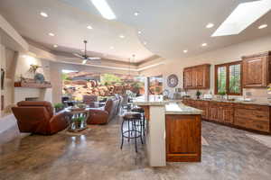 Kitchen featuring a tray ceiling, a kitchen bar, brown cabinetry, recessed lighting, and tasteful backsplash
