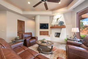 Living area with a ceiling fan, a tray ceiling, a large fireplace, and recessed lighting