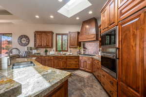 Kitchen with a skylight, tasteful backsplash, recessed lighting, premium range hood, and stainless steel appliances