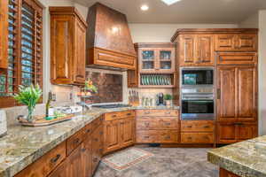 Kitchen featuring brown cabinets, custom range hood, built in appliances, backsplash, and recessed lighting