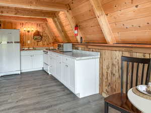 Kitchen with white cabinetry, wood walls, freestanding refrigerator, dark wood finished floors, and wooden ceiling