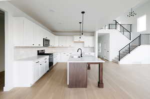 Kitchen featuring white cabinetry, a kitchen breakfast bar, appliances with stainless steel finishes, an island with sink, and pendant lighting
