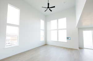 Unfurnished living room featuring a high ceiling, light wood-style flooring, ceiling fan, and plenty of natural light