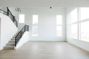 Unfurnished living room featuring light wood-style flooring, stairway, and a high ceiling