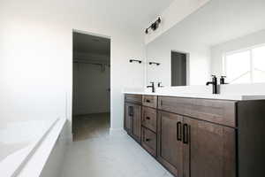 Bathroom with double vanity, a walk in closet, light marble finish flooring, and a garden tub