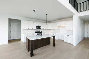 Kitchen with white cabinetry, a kitchen bar, a kitchen island with sink, hanging light fixtures, and tasteful backsplash