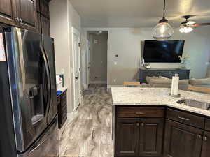 Kitchen featuring dark brown cabinets, stainless steel fridge, light stone counters, decorative light fixtures, and light wood-type flooring