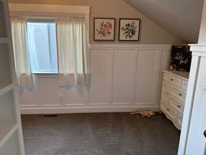 Bonus room featuring a decorative wall, dark carpet, wainscoting, and vaulted ceiling