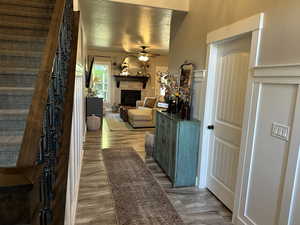 Living area featuring stairs, a fireplace, a ceiling fan, and light wood-type flooring
