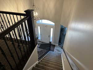 Foyer entrance with dark colored carpet, a towering ceiling, a chandelier, and stairs