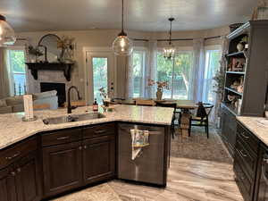 Kitchen featuring dark brown cabinetry, a fireplace, stainless steel dishwasher, light stone countertops, and decorative light fixtures