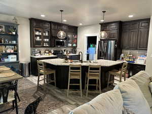 Bar featuring tasteful backsplash, dark brown cabinets, stainless steel appliances, glass insert cabinets, and light stone counters