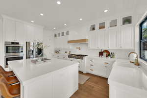 Kitchen with white cabinetry, custom exhaust hood, recessed lighting, light stone countertops, and stainless steel appliances