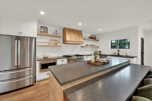 Kitchen featuring stainless steel appliances, dark countertops, premium range hood, recessed lighting, and light wood-style flooring