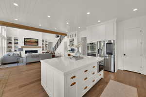 Kitchen with white cabinets, a large fireplace, stainless steel appliances, a kitchen island, and open floor plan