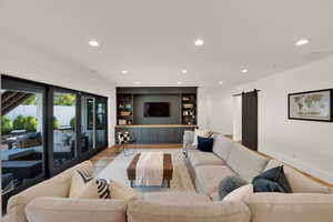 Living room featuring a barn door, recessed lighting, light wood-style floors, and built in features